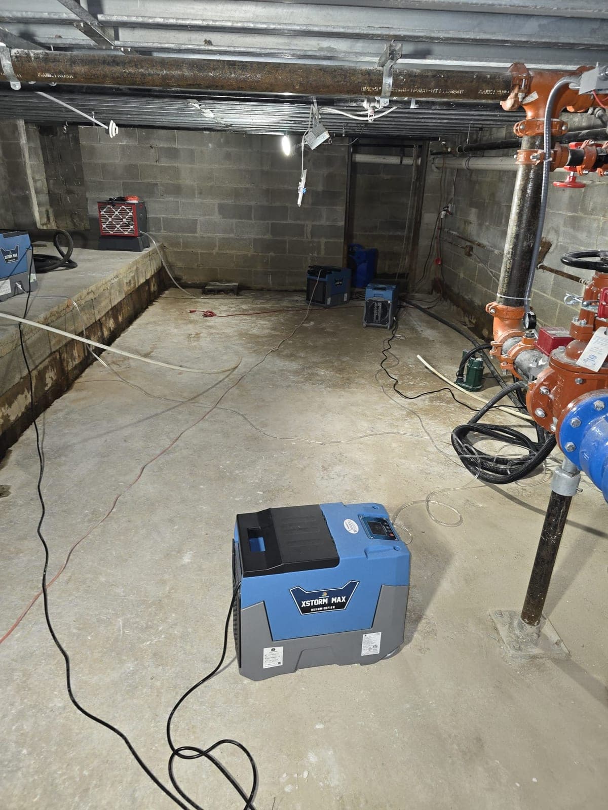 Commercial dehumidifiers and an air scrubber set up to dry a concrete block basement after water damage